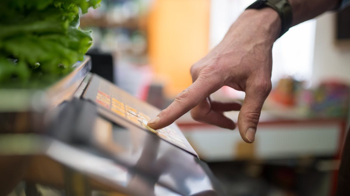 A hand interacting with a digital weighing scale in a produce section, emphasizing technology in shopping.